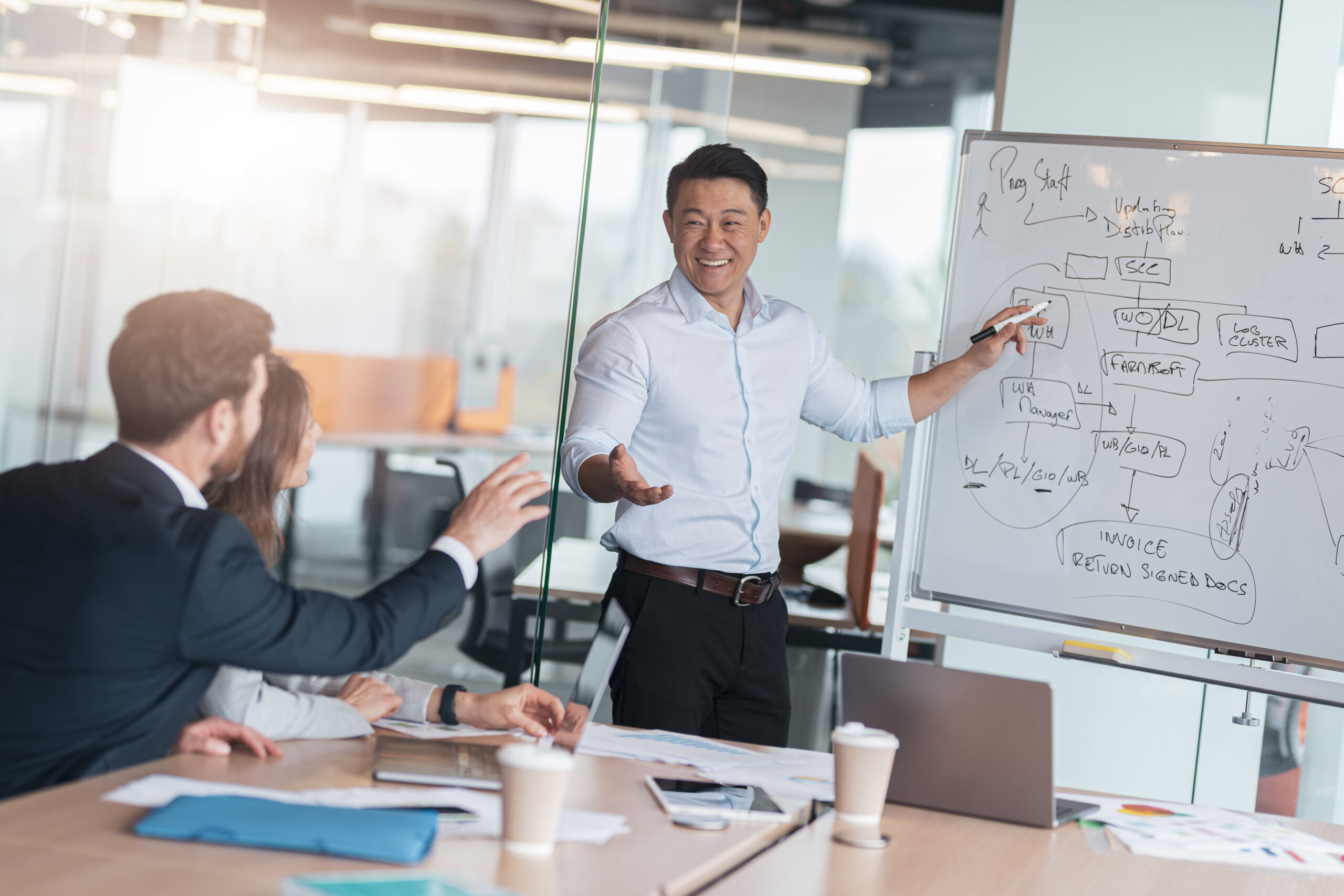 Mature asian coach or speaker make flip chart presentation to diverse businesspeople at meeting.